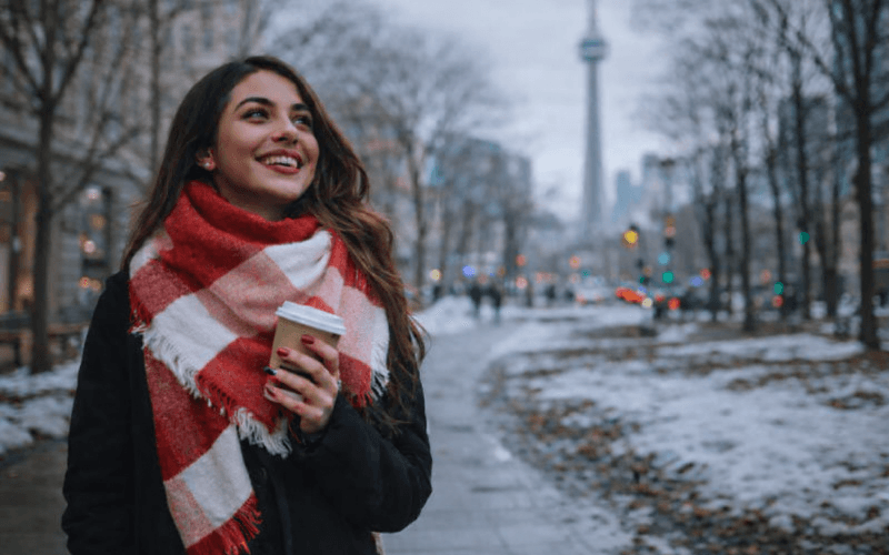 International student in Toronto holding a coffee and smiling on a winter city street, representing confidence and career readiness in Canada