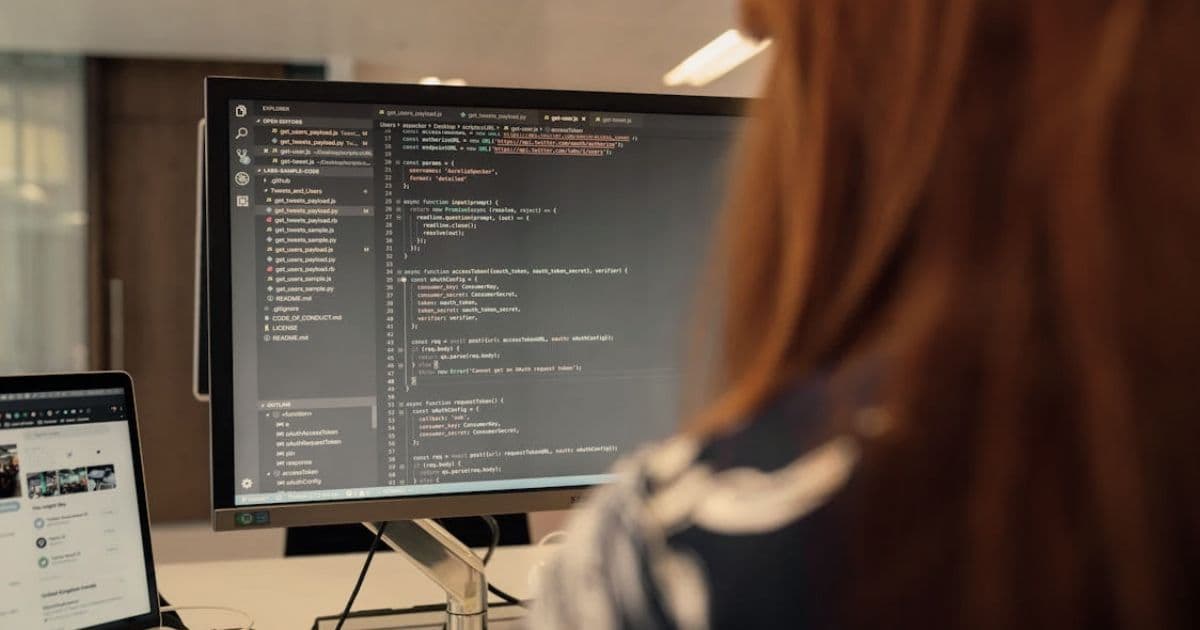 Software developer reviewing resume template on laptop with code editor and GitHub profile visible on second monitor