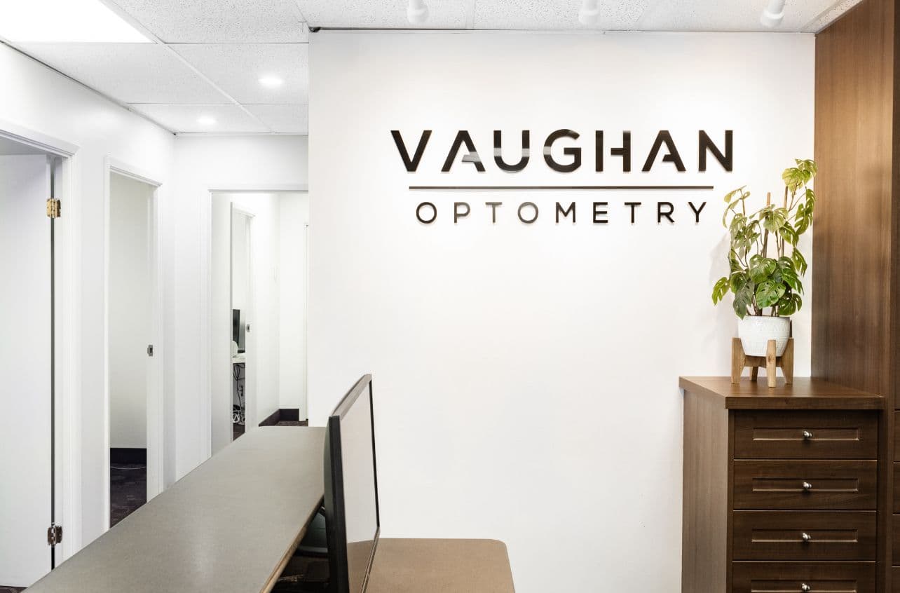 Optometry clinic team reviewing patient feedback together at the front desk, with an eye care reception area visible in the background