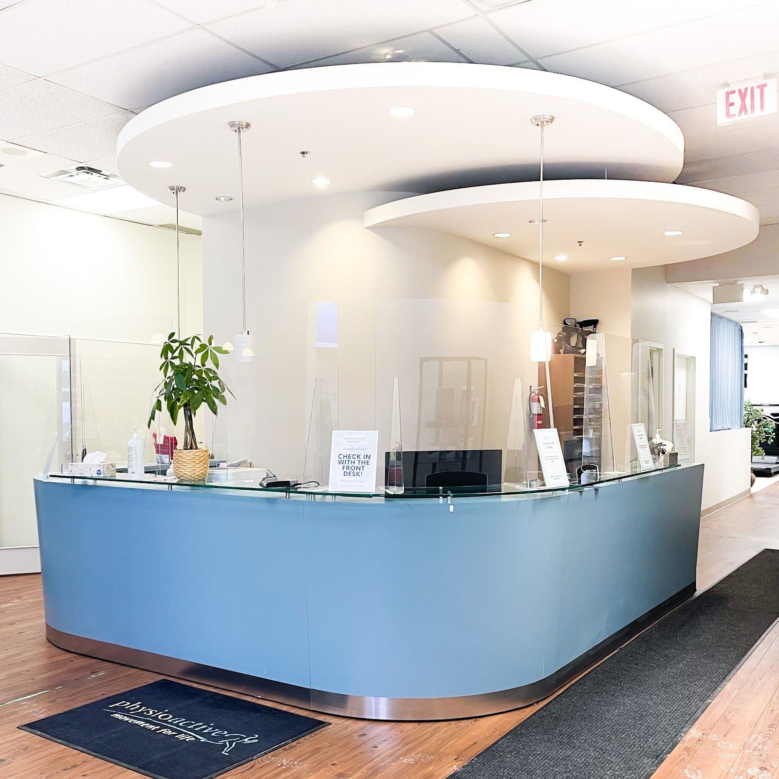 PhysioActive clinic team reviewing patient feedback together at the front desk, with a tablet showing Google reviews in a bright, welcoming reception area