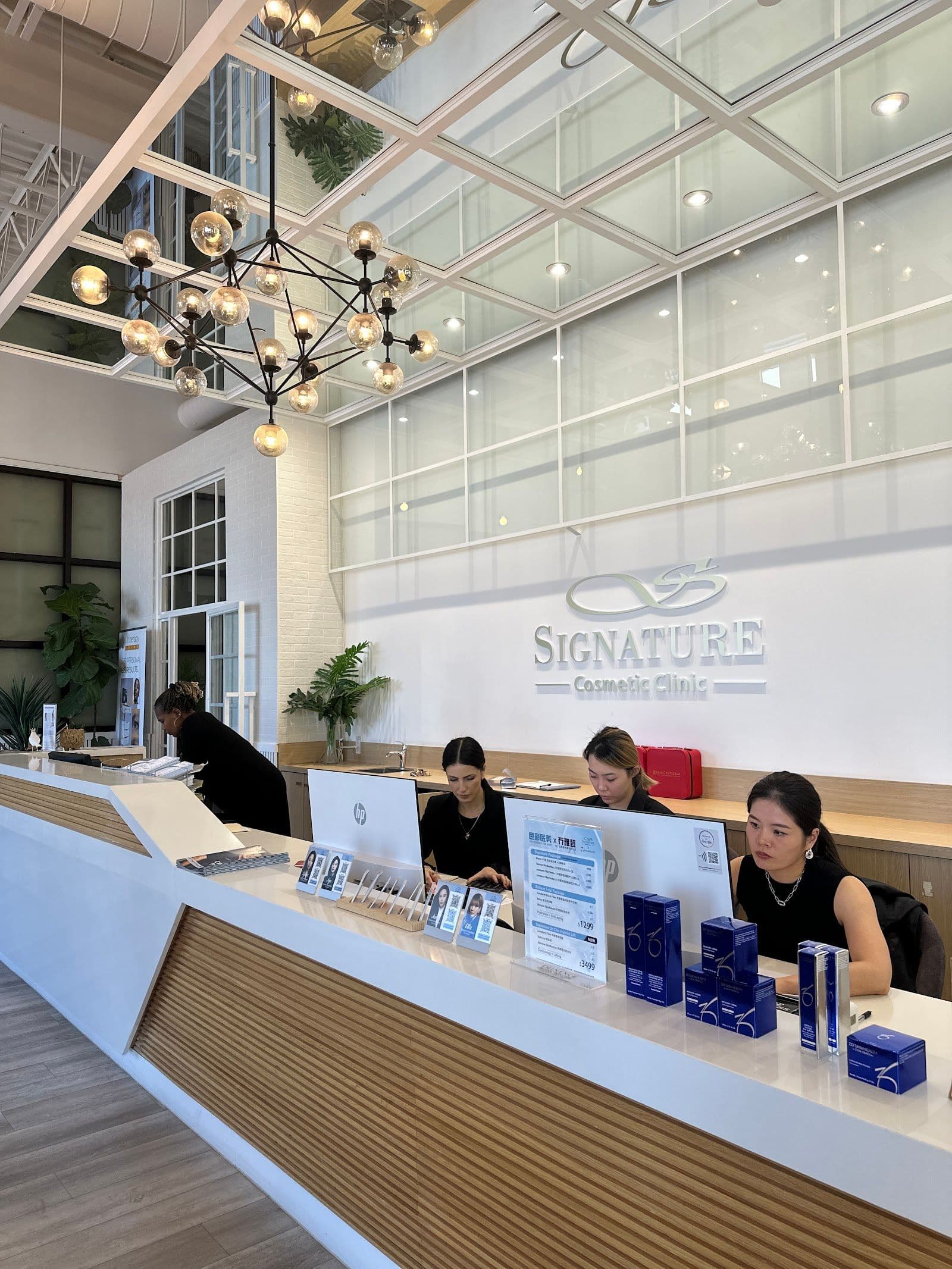 Aesthetic clinic consultant and front desk team reviewing patient feedback together at a reception desk inside a cosmetic clinic