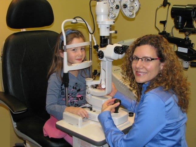 Optometry clinic front desk team reviewing patient feedback on a tablet together in a bright, tidy reception area